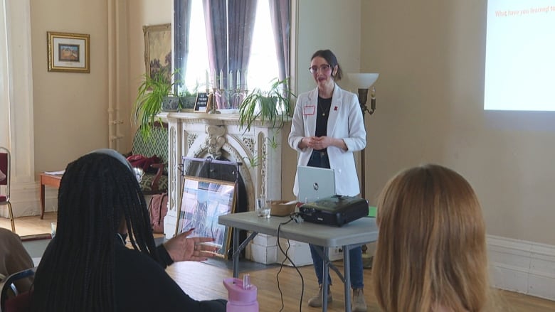 Woman in white coat speaking to group.