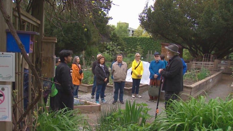 A man carrying a cane talks to people in a community garden.