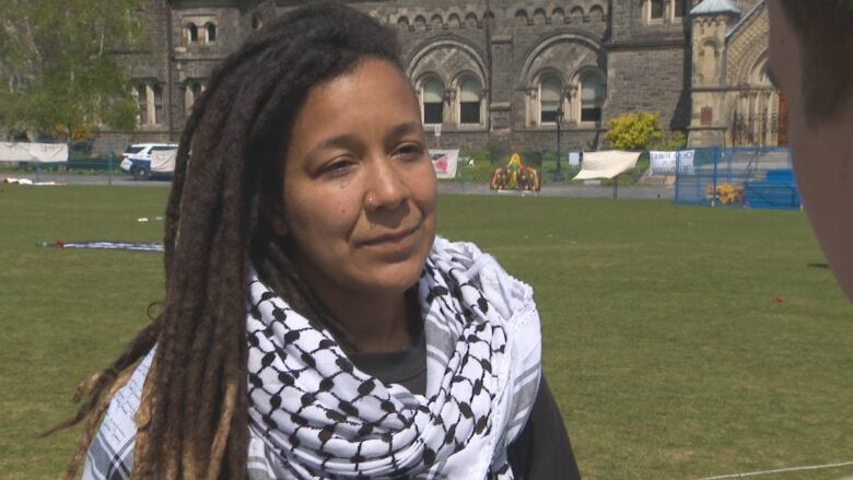 An woman stands in a grass field wearing a keffiyeh.