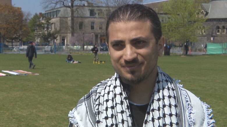 A man stands in a grass field with a keffiyeh.