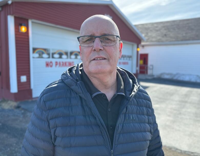 A person wearing a jacket stands in front of a fire hall.