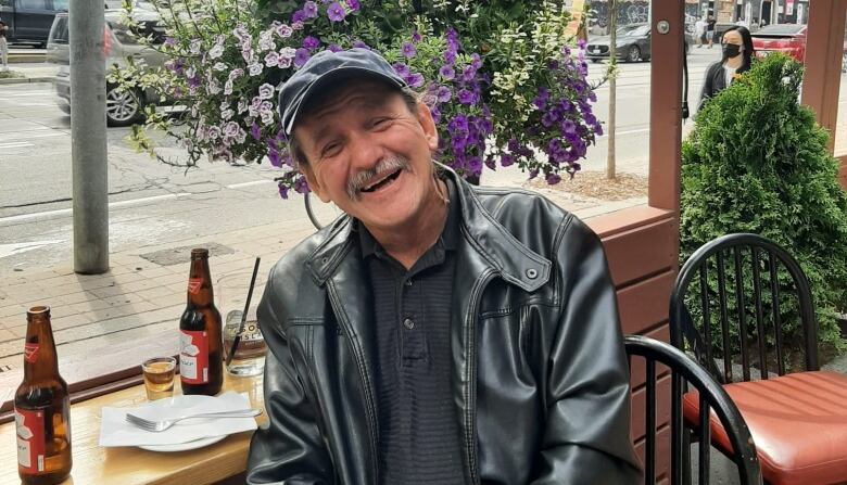 A man smiles at the camera in front of flowers. 