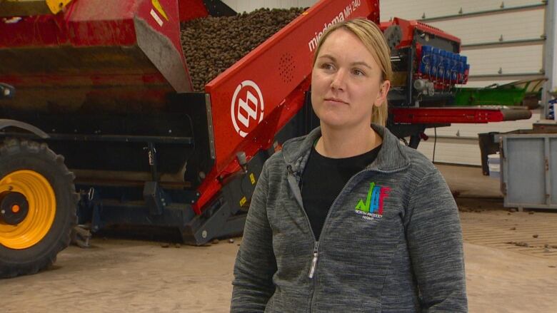 A woman wearing a sweater stands in front of farm equipment.