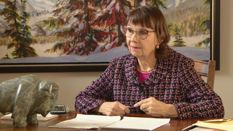 A woman wearing a blazer sits at a desk.