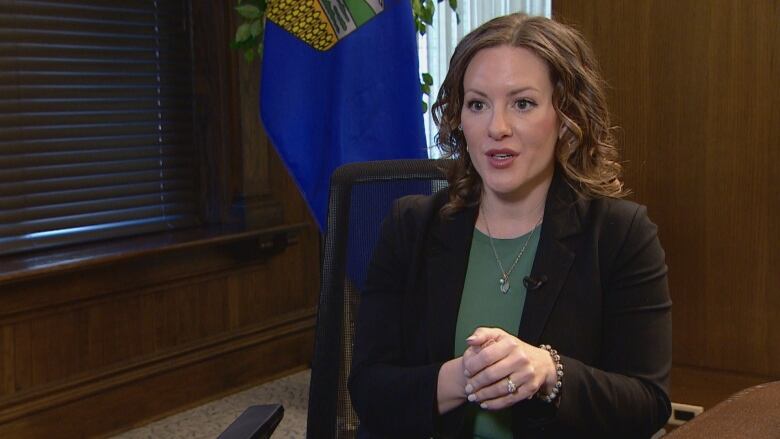 A woman sits in a chair in front of an Alberta flag.