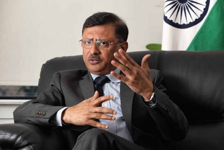 Sanjay Kumar Verma, a man in his 50s is pictured sitting in a chair wearing a grey suit gesturing with his hands as he speaks