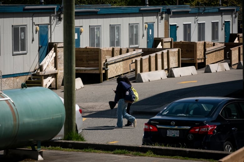 Two high school students are seen walking past a string of portable classrooms installed in their school's parking lot. 