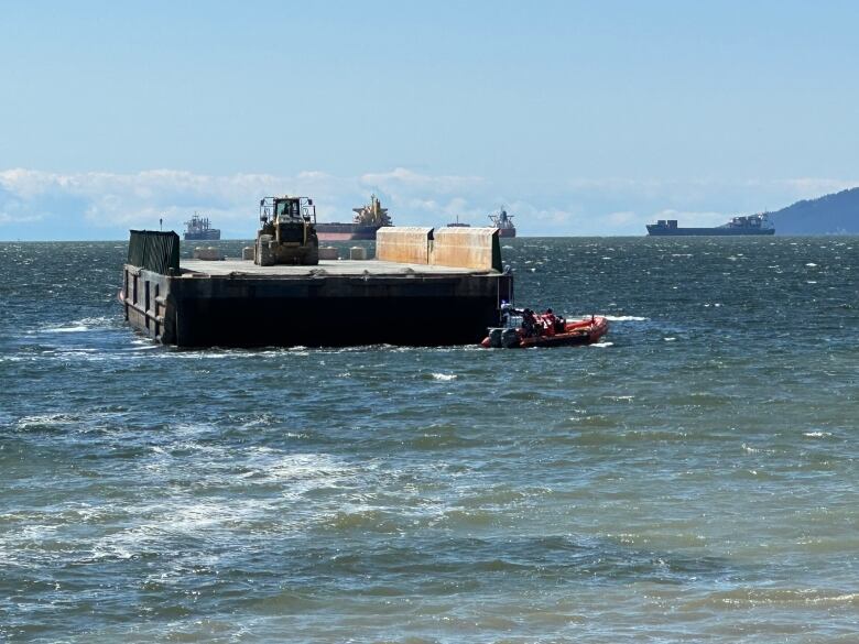 A large barge is seen being pulled by tow boats on a picturesque day.