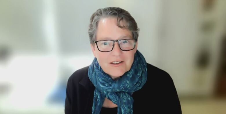 A woman wearing glasses, a blue scarf and black shirt is pictured looking at a video computer.