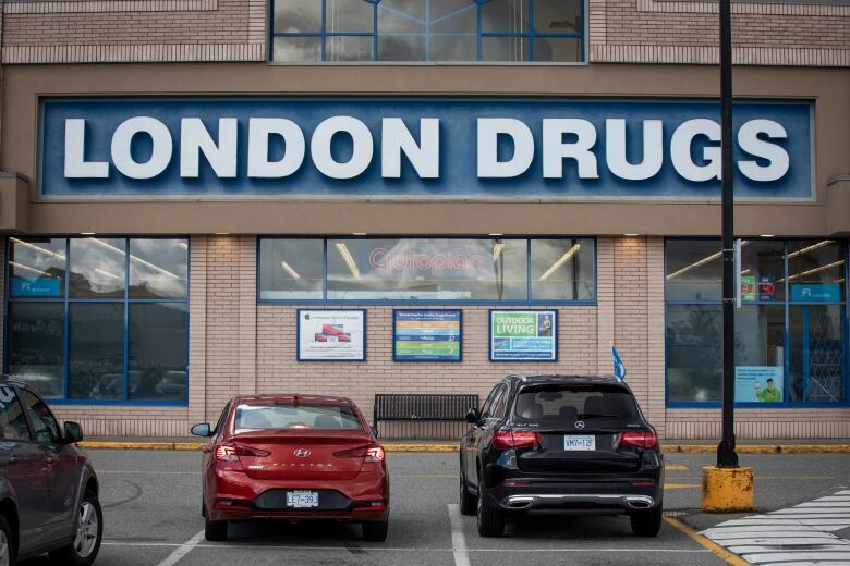 A store sign with cars parked front of it, with the sign reading 'London Drugs'.