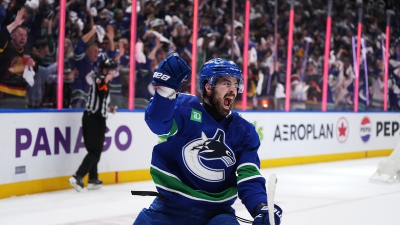 A hockey player wearing blue celebrates after scoring goal.