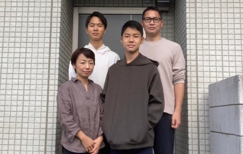 Four people -- two young men along with an older man and an older woman -- pose on the steps in front of a home.