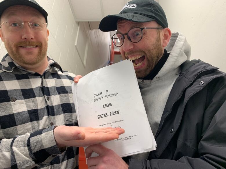 Two men hold up a movie script 