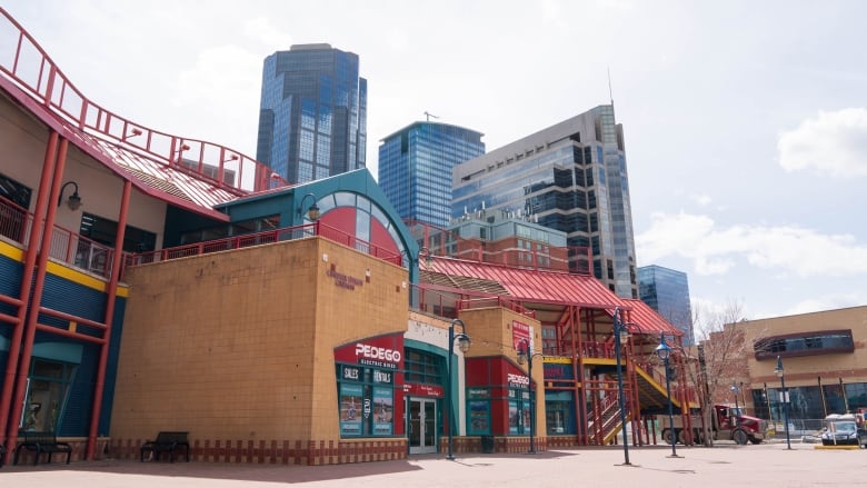 a red teal and yellow building with orange brick stands in an outdoor plaza. there are large skyscrapers in the background.