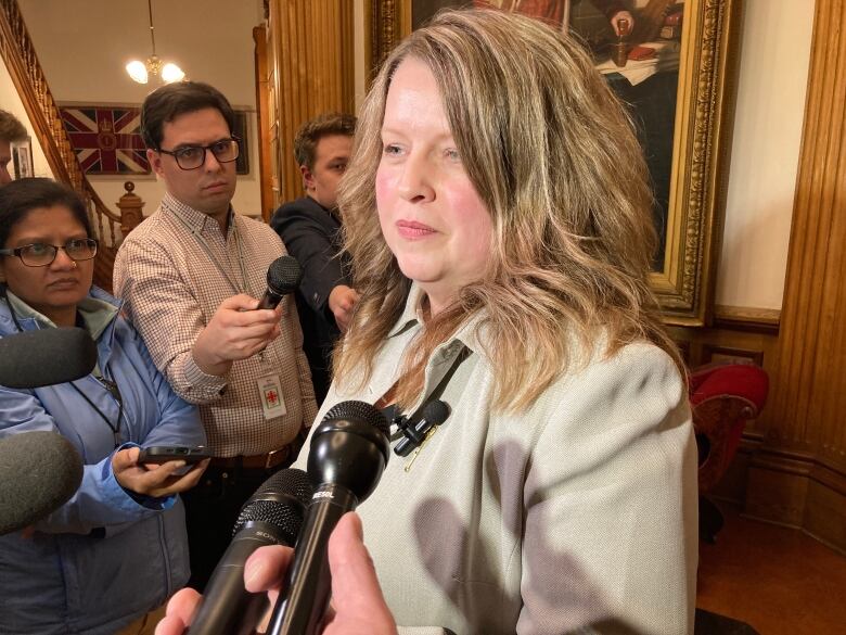 Woman surrounded by reporters holding microphones