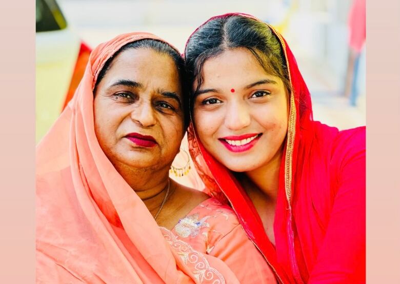 A young woman and an older woman in bright clothing smile as they pose for the camera. 