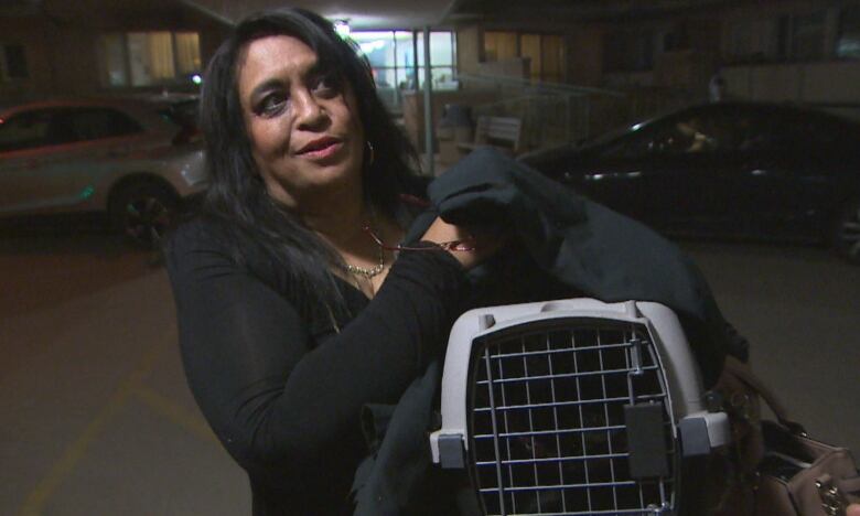 A woman with long black hair holds a pet carrier.