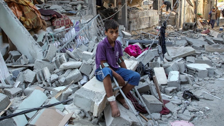 A wounded child in a purple T-shirt sits on debris at the site of an Israeli strike on a house.