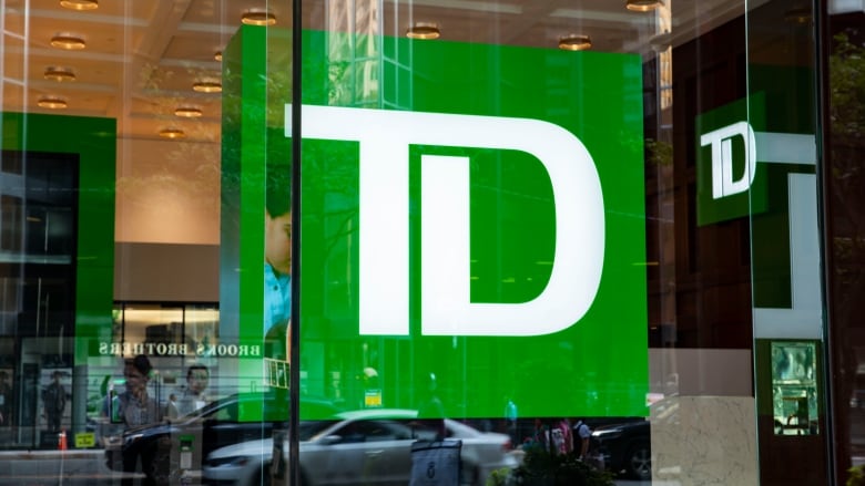 A close up of a large TD logo behind a glass window on a street. 