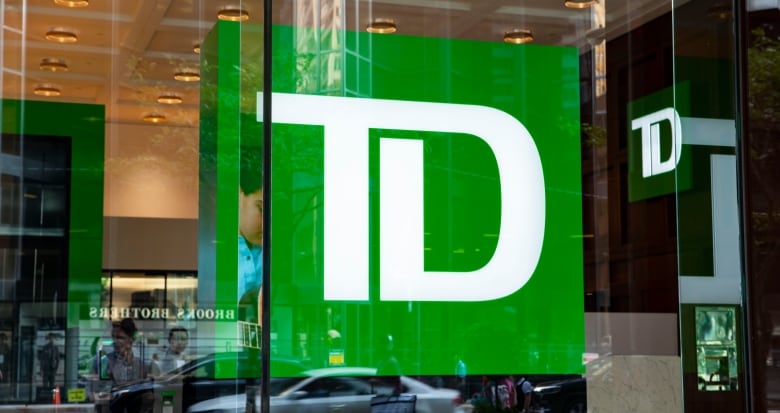 A close up of a large TD logo behind a glass window on a street. 