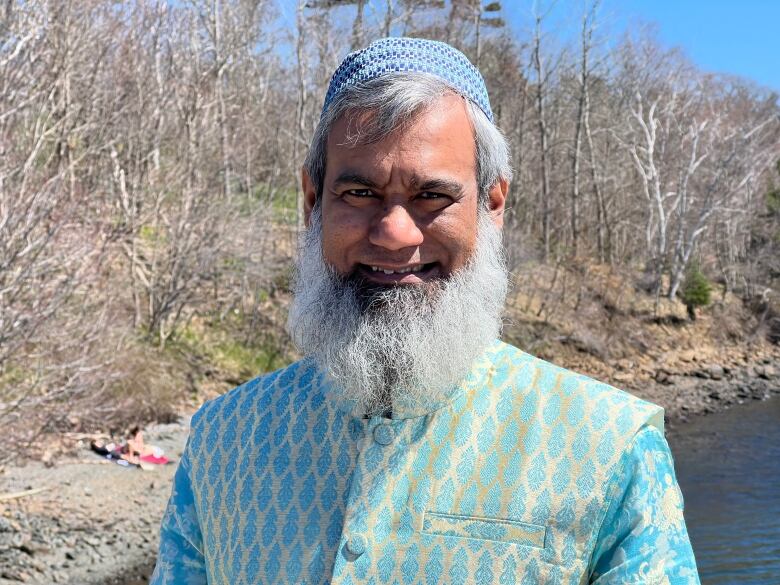 A man with a bear is seen wearing an aqua and gold traditional Bangladeshi outfit.