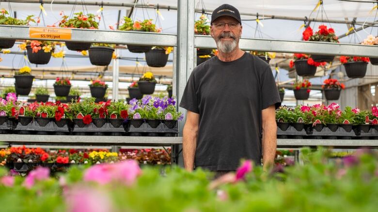 A man stands by flowers in a greenhouse.