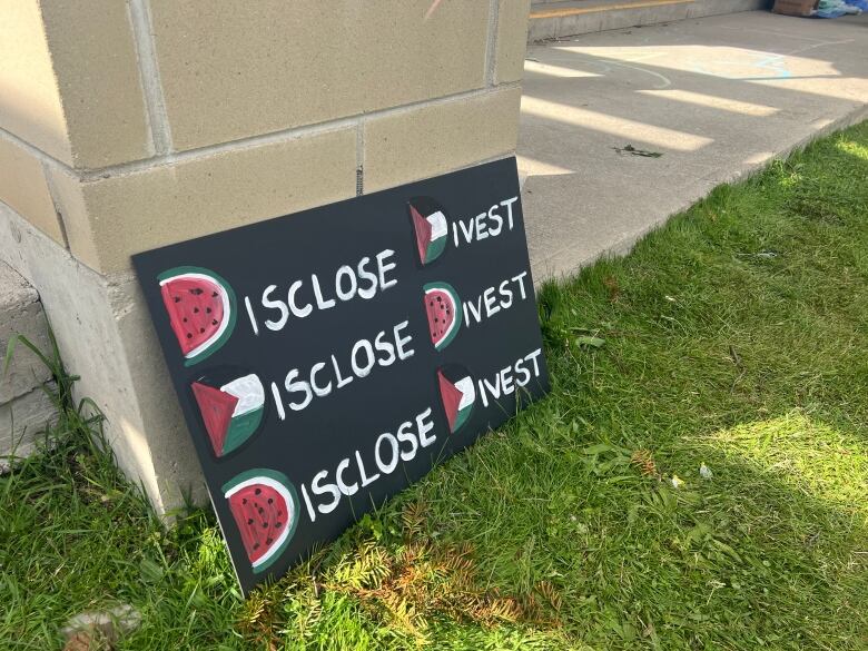 A painted protest sign says Disclose, Divest, Disclose, Divest, Disclose, Divest