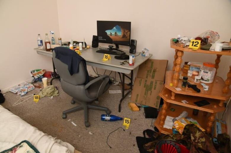 A computer desk in a messy room with yellow evidence markers in several places.