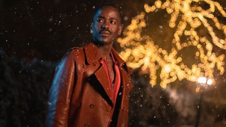 A man wearing a brown leather coat stands in the snow.