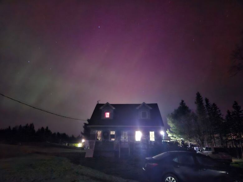 A lit house in the foreground with northern lights behind.