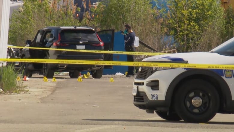 Car surrounded by a police tape with a police cruiser on the right. 