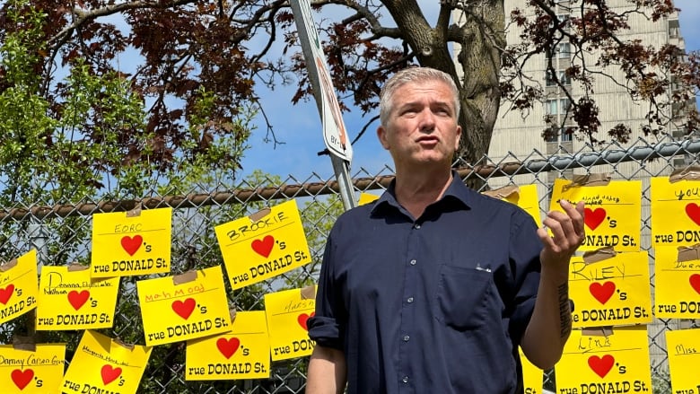 A man stands in a park addressing a crowd. 