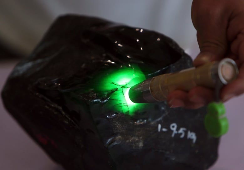 A person shines a flashlight on a green piece of rock, which is jade.