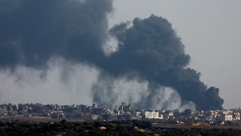 Black smoke billows above a city populated with destroyed buildings.