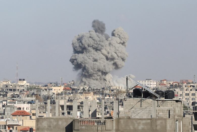 A plume of grey smoke rises above densely packed concrete buildings. 