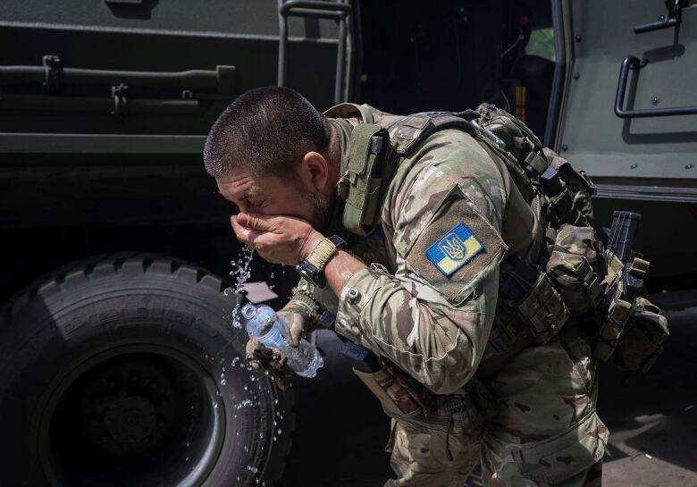 A Ukrainian soldier wearing a camouflage uniform washes his face from a bottle of water.