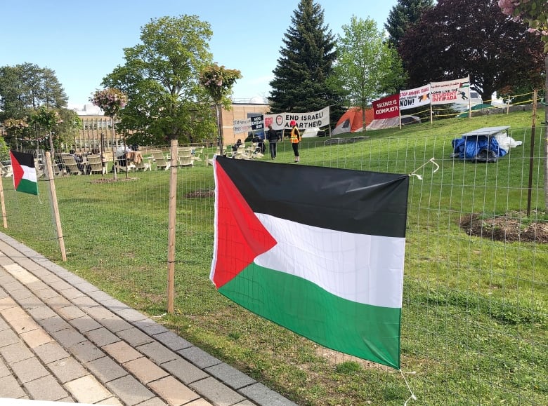 Palestine flag hung on makeshift fence, demonstrators are visible in the background