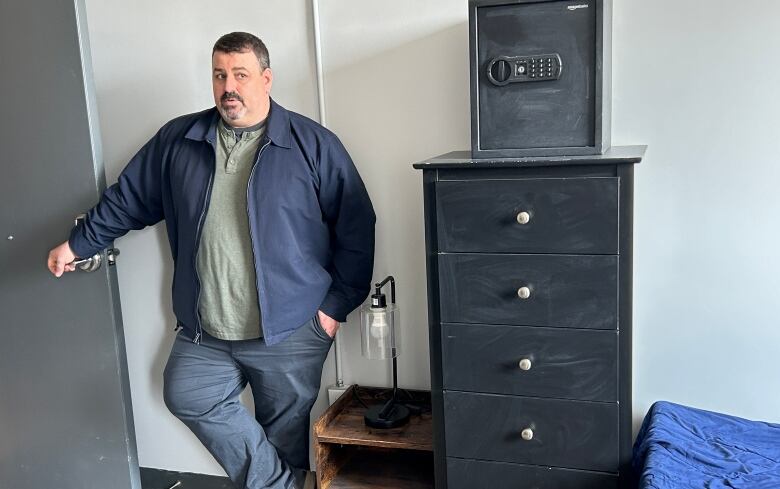 A man stands next to the door of a bedroom with his hand on the knob