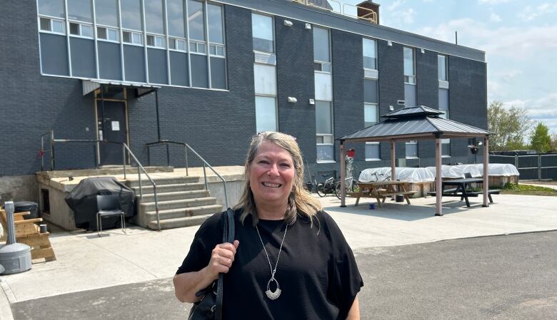 A woman stands in front of a large grey building. 