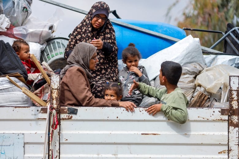 Two women and four young children ride in the back of a white pickup truck as they evacuate a city in Gaza.