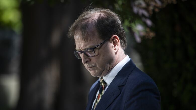 A man wearing a patterned tie looks down.