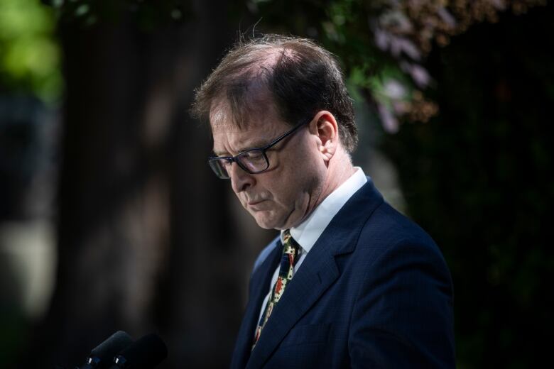 A man wearing a patterned tie looks down.