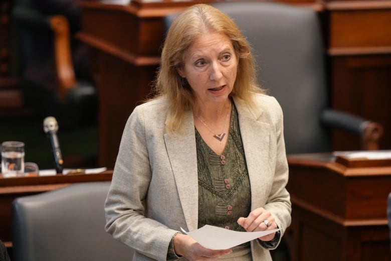 A woman wearing a green blouse holding a paper in a large room.