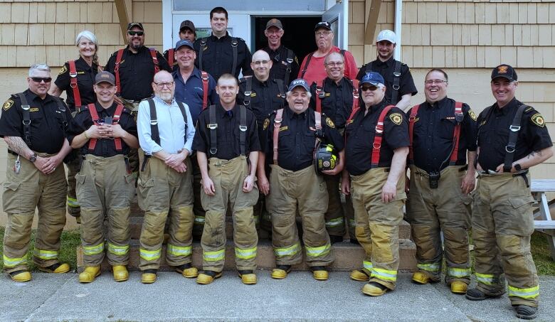 Firefighters are shown wearing coveralls and navy blue shirts underneath outside a community centre.