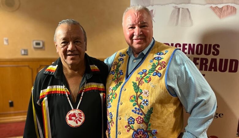 Two men, one in a First Nations ribbon shirt the other in a Mtis beaded vest, pose for a picture.