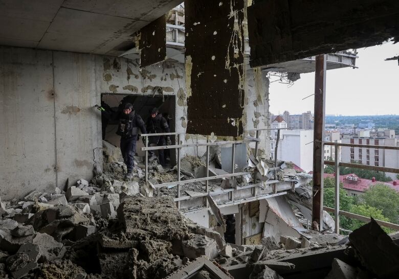 Two helmeted workers are seen walking in the rubble inside an residential highrise, with the windows gone from a destroyed unit.