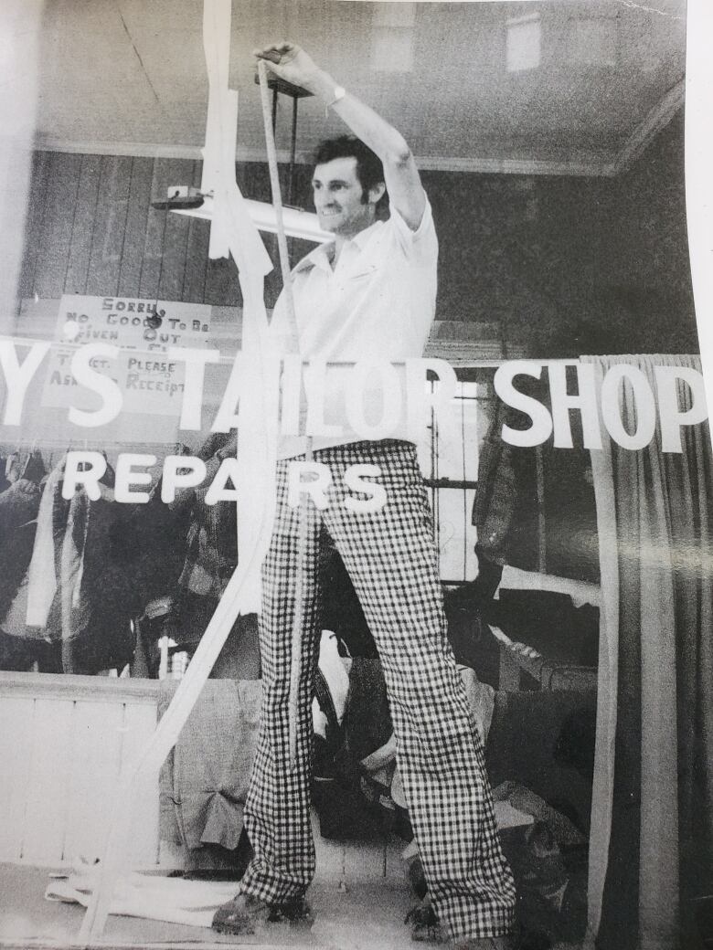 A black and white image of a man fixing a window, on which can be read 'Tailor Shop.'