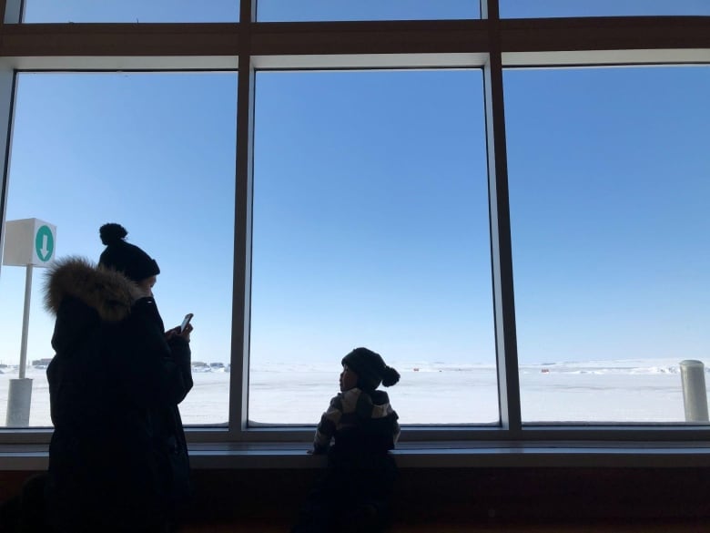 A little kid and an adult look out a window of an airport