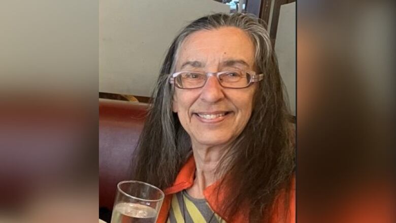 A woman with glasses smiles while holding a glass of water.