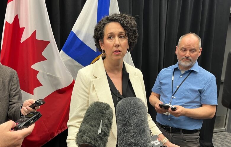 A woman stands in front of microphones while other people stand around her.